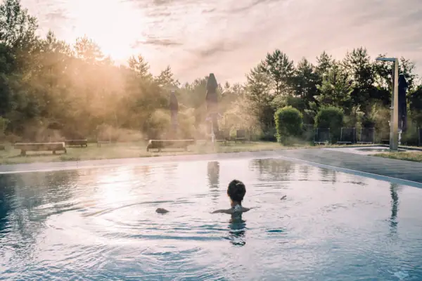 Eine Frau in einem Pool mit Bäumen und bewölktem Himmel.