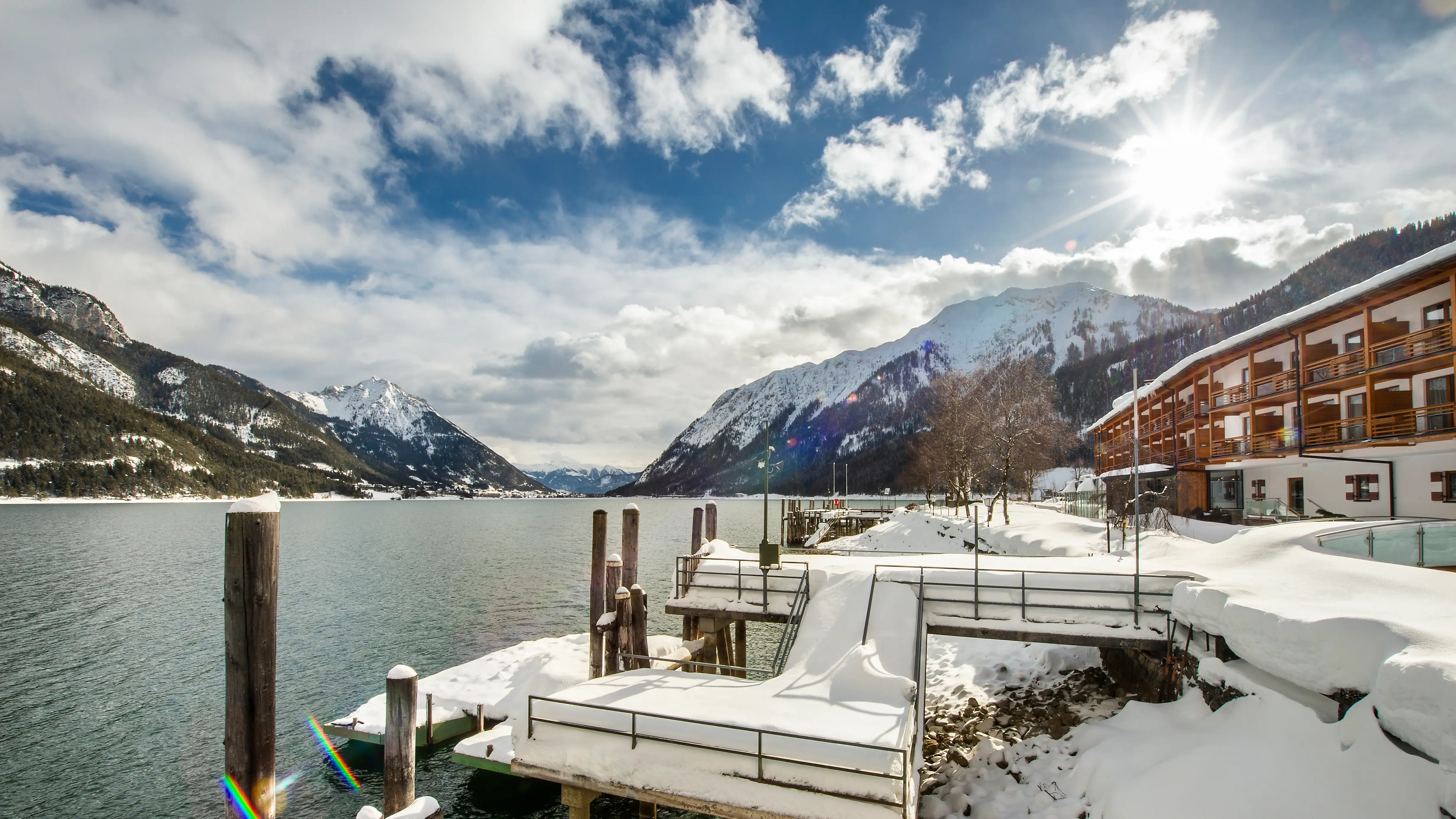 Schneebedeckter Steg an einem See mit Bergen im Hintergrund.