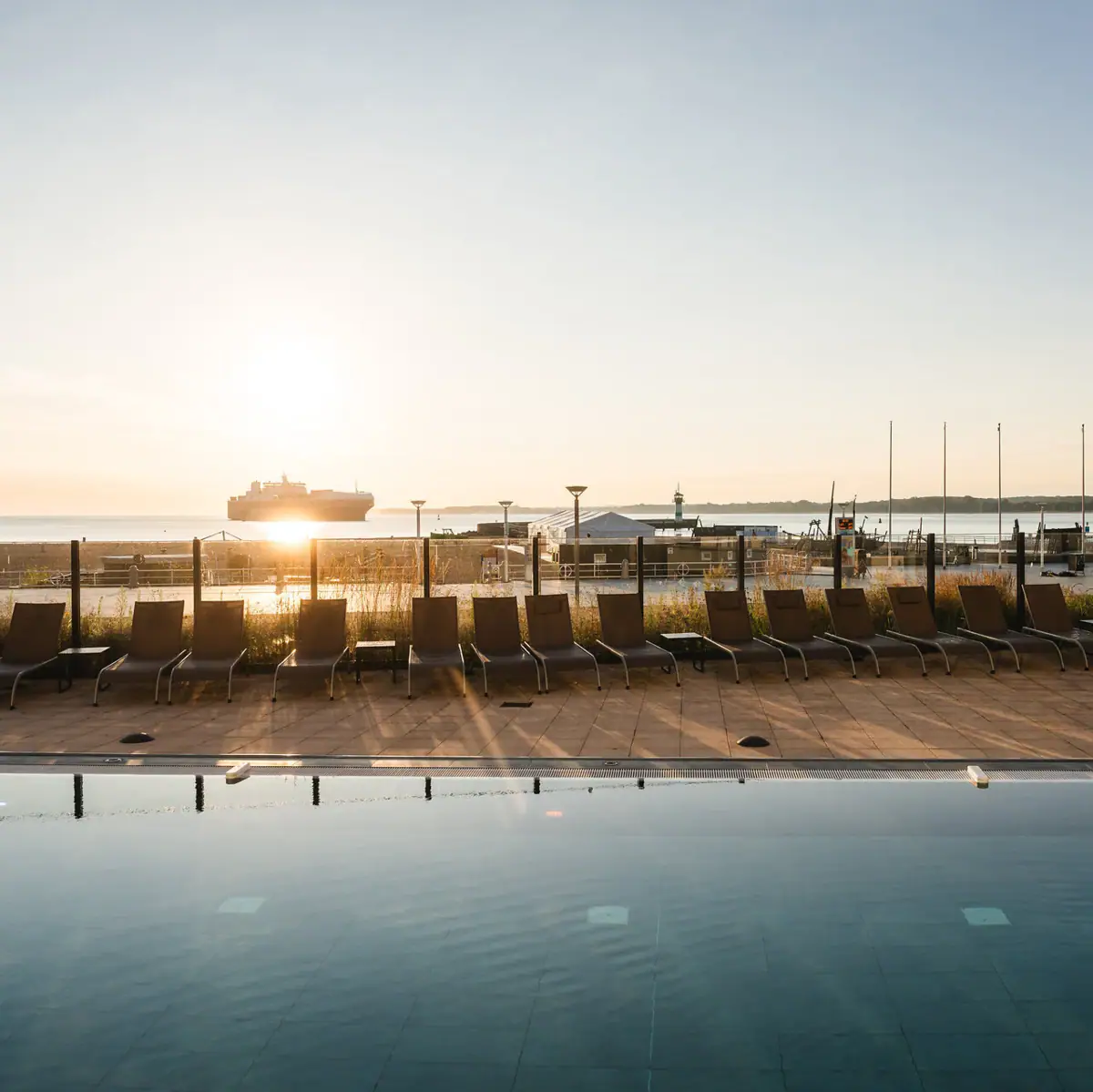 Ein Pool mit Stühlen und einem Boot im Hintergrund.