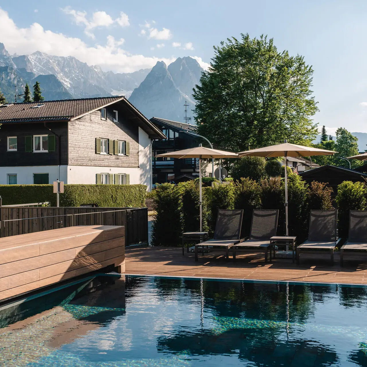 Pool mit Liegestühlen und Sonnenschirmen neben einem Haus