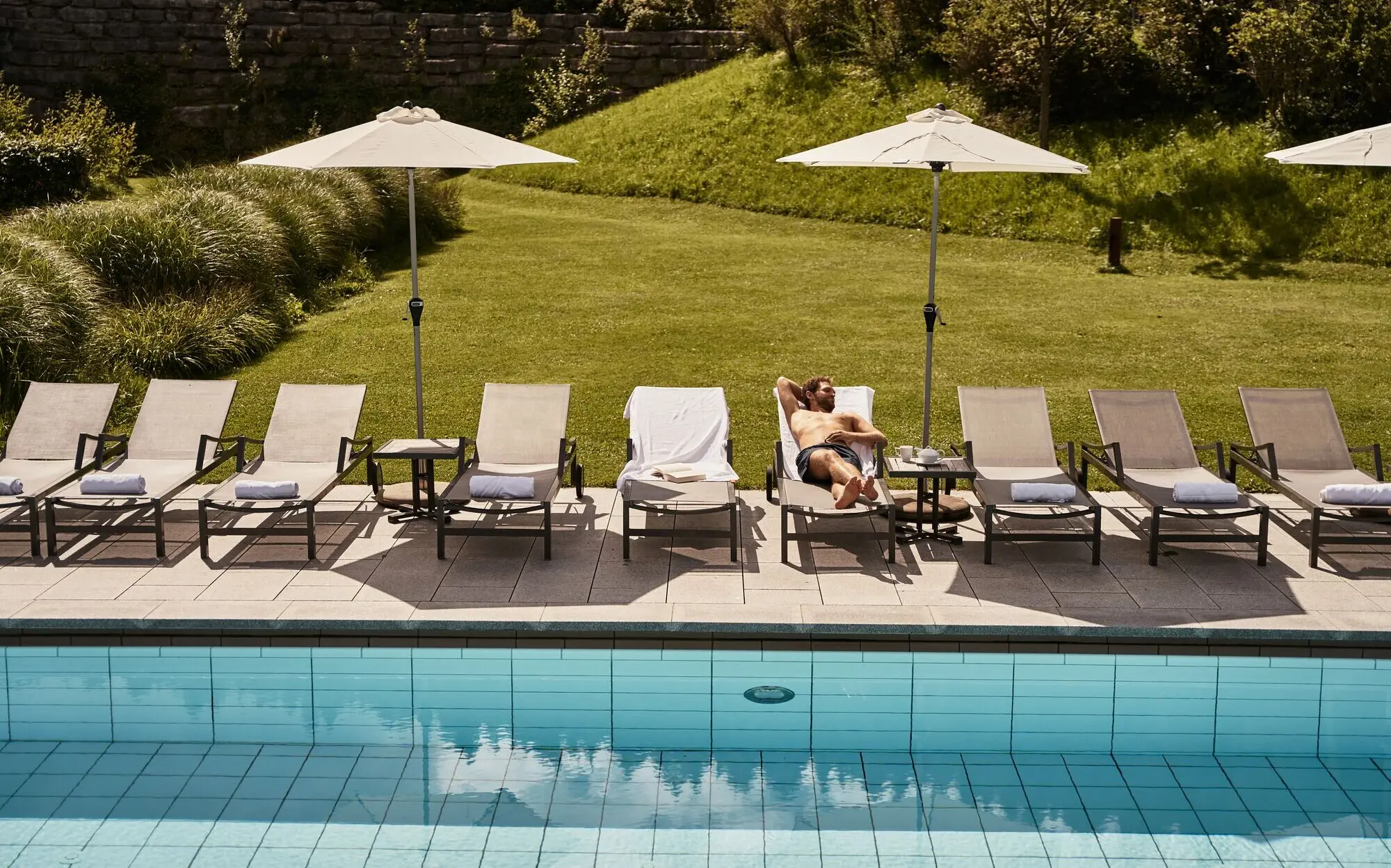 Mann liegt auf einer Sonnenliege neben einem Swimmingpool.