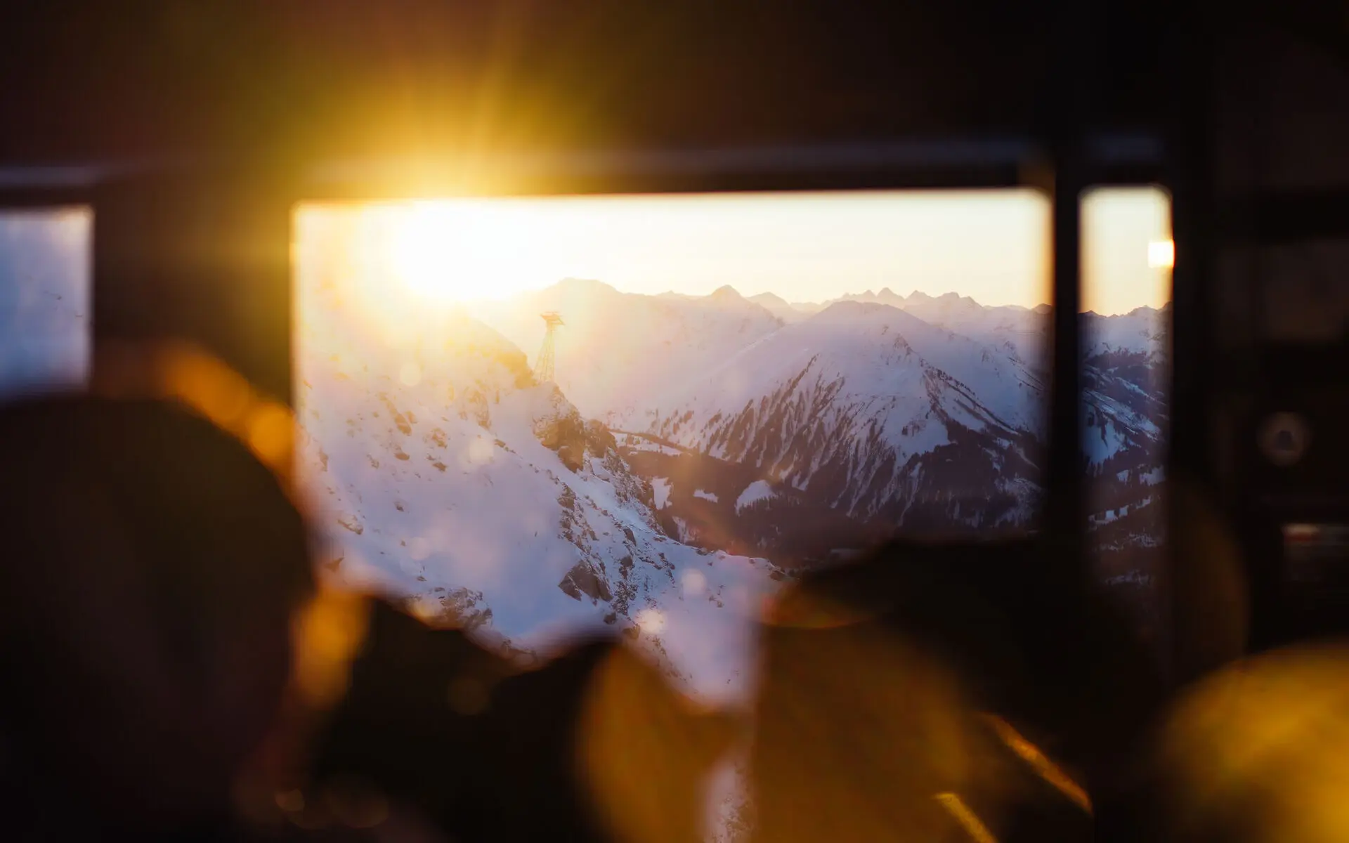 Sonne scheint durch ein Fenster einer Gondel auf eine verschneite Berglandschaft.