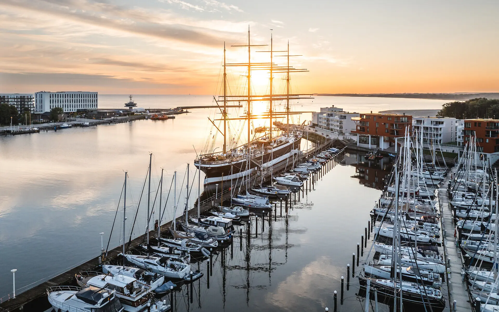 Großes Schiff im Hafen bei Sonnenaufgang, umgeben von Wasser und leicht bewölktem Himmel.