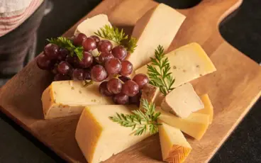 A cheese platter with red grapes on a wooden board.