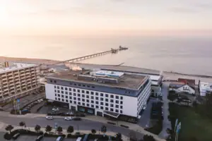 aja Grömitz Ein Gebäude neben einem Gewässer unter einem wolkigen Himmel.