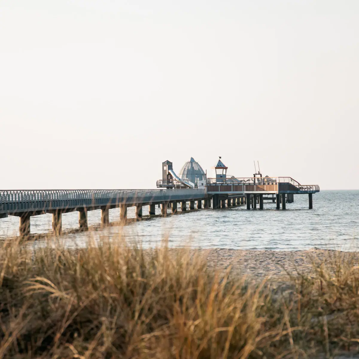 Seebrücke Langer Pier am Strand mit Gras im Vordergrund.