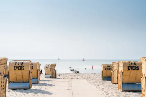 Strand mit vielen Strandkörben und einem Gewässer im Hintergrund.