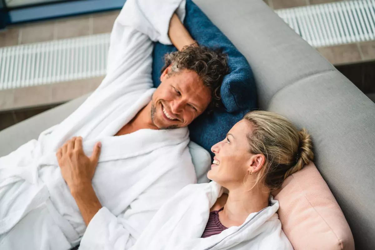 SPA Ein Mann und eine Frau liegen lächelnd auf einem Sofa.