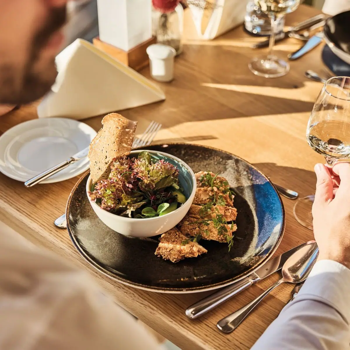 Feinspitz Restaurant Mann isst Salat und trinkt ein Glas Wein am Tisch.