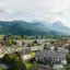 Stadtansicht mit vielen Gebäuden, Bäumen und Bergen im Hintergrund.