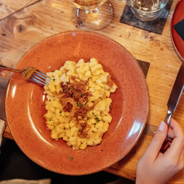Käsespätzle Ein Teller mit Makkaroni und Käse, daneben eine Gabel und ein Messer.
