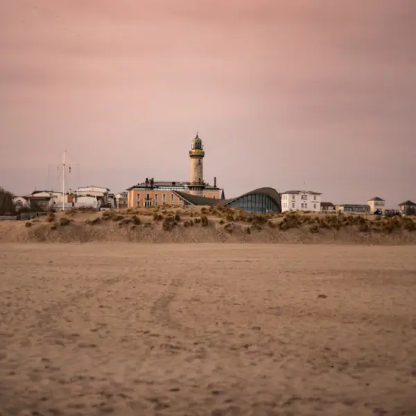 Warnemünde Ein Leuchtturm in der Ferne auf einem sandigen Gelände.
