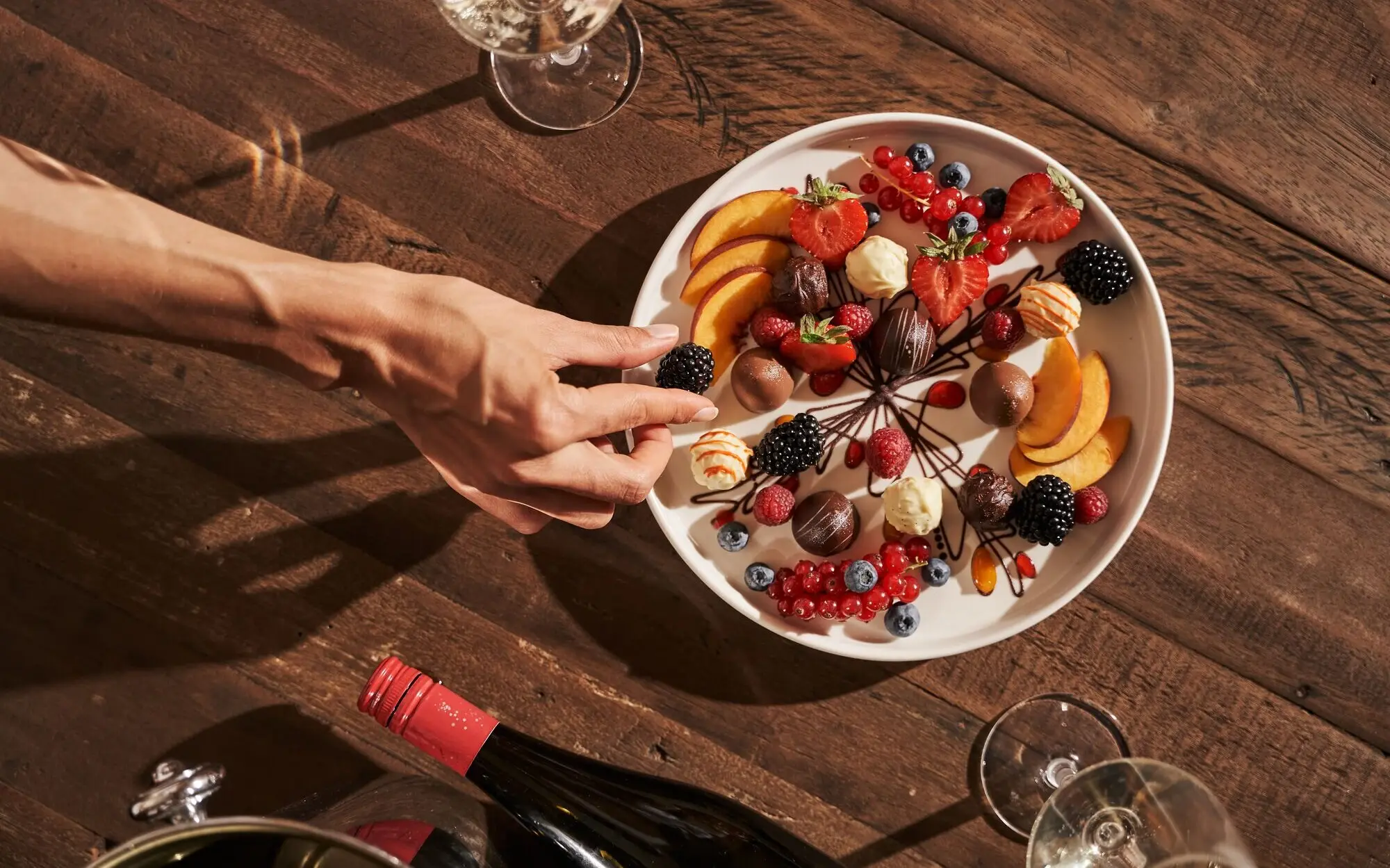 Hand greift nach einem Teller mit Obst auf einem Tisch.