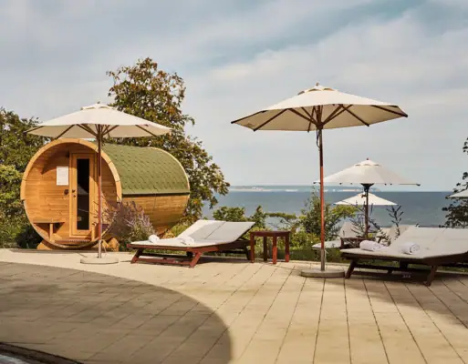 Deckstühle und Sonnenschirme neben einem Fass und einem Gewässer.