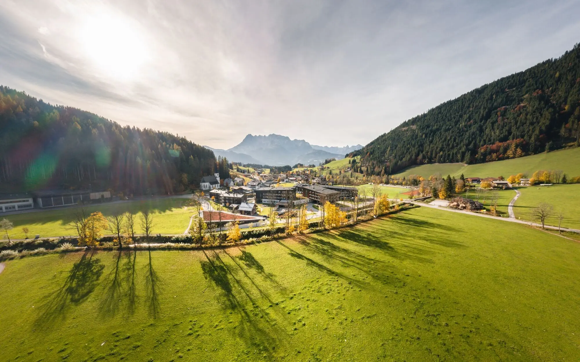 Grünes Tal zwischen Bergen mit Bäumen und vereinzelten Gebäuden im Hintergrund.