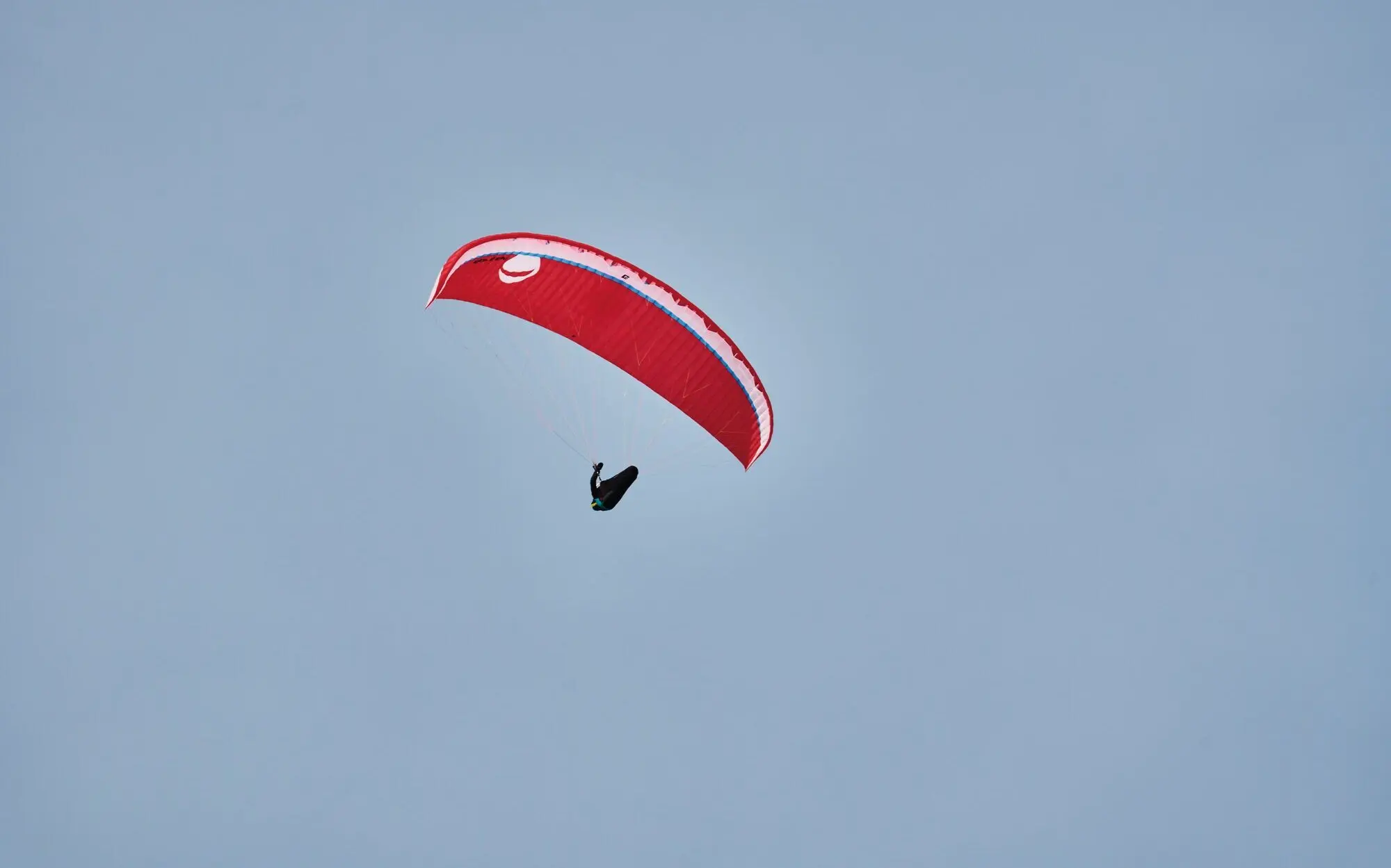 Person paragliding with a red glider in front of the blue sky.