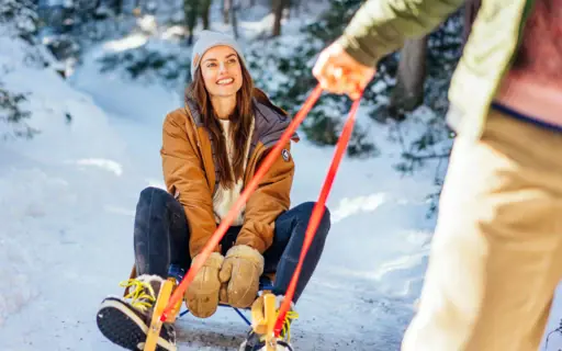 Frau zieht einen Mann auf einem Schlitten im Schnee.