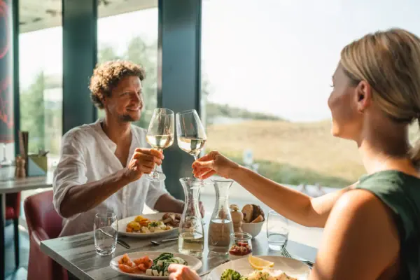 Ein Mann und eine Frau stoßen mit Weingläsern an einem Tisch an.