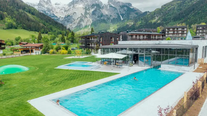 Schwimmbecken mit einem Gebäude und Bergen im Hintergrund.