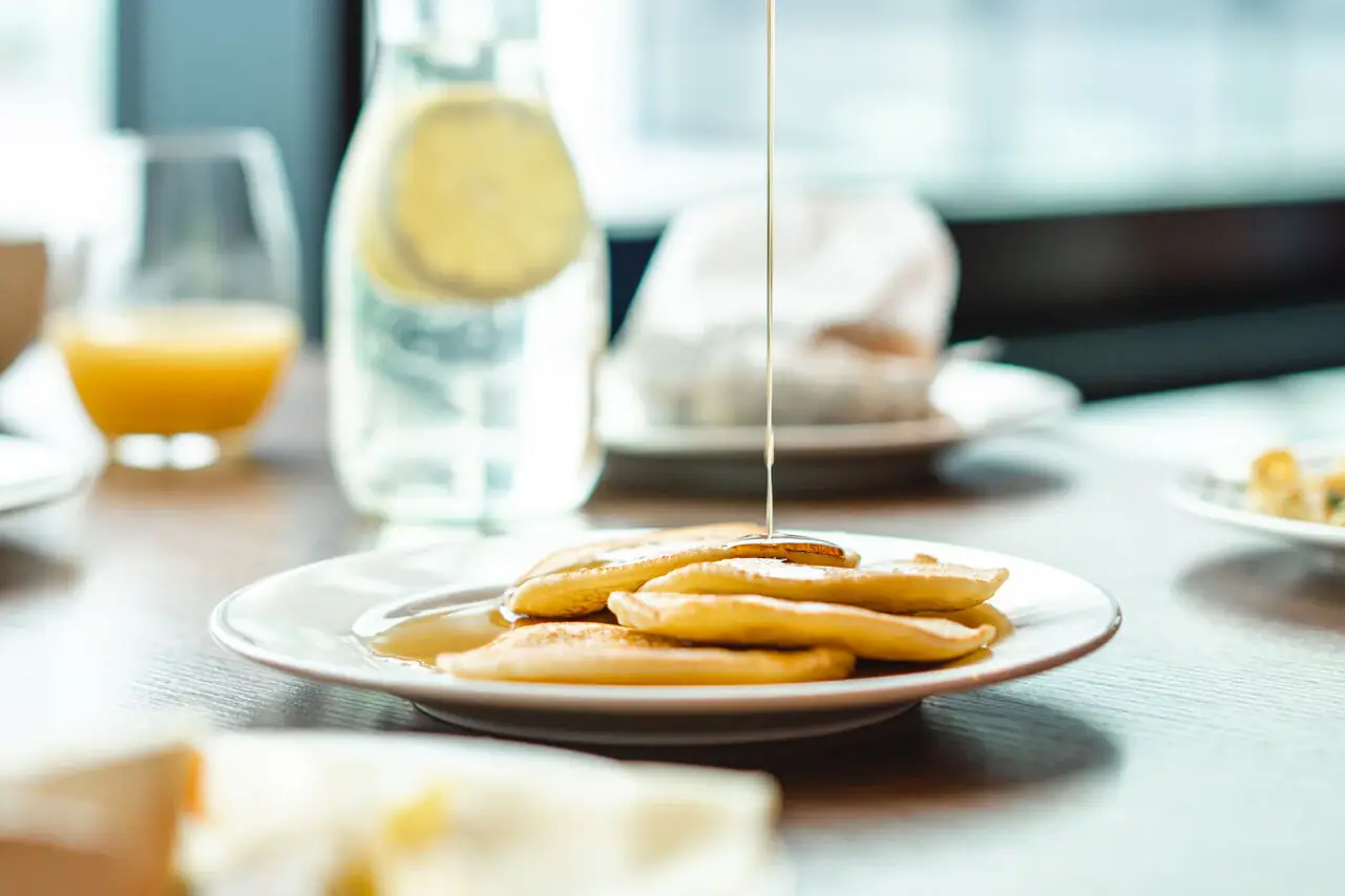 Pancakes Eine Person gießt Sirup auf einen Teller mit Pfannkuchen.