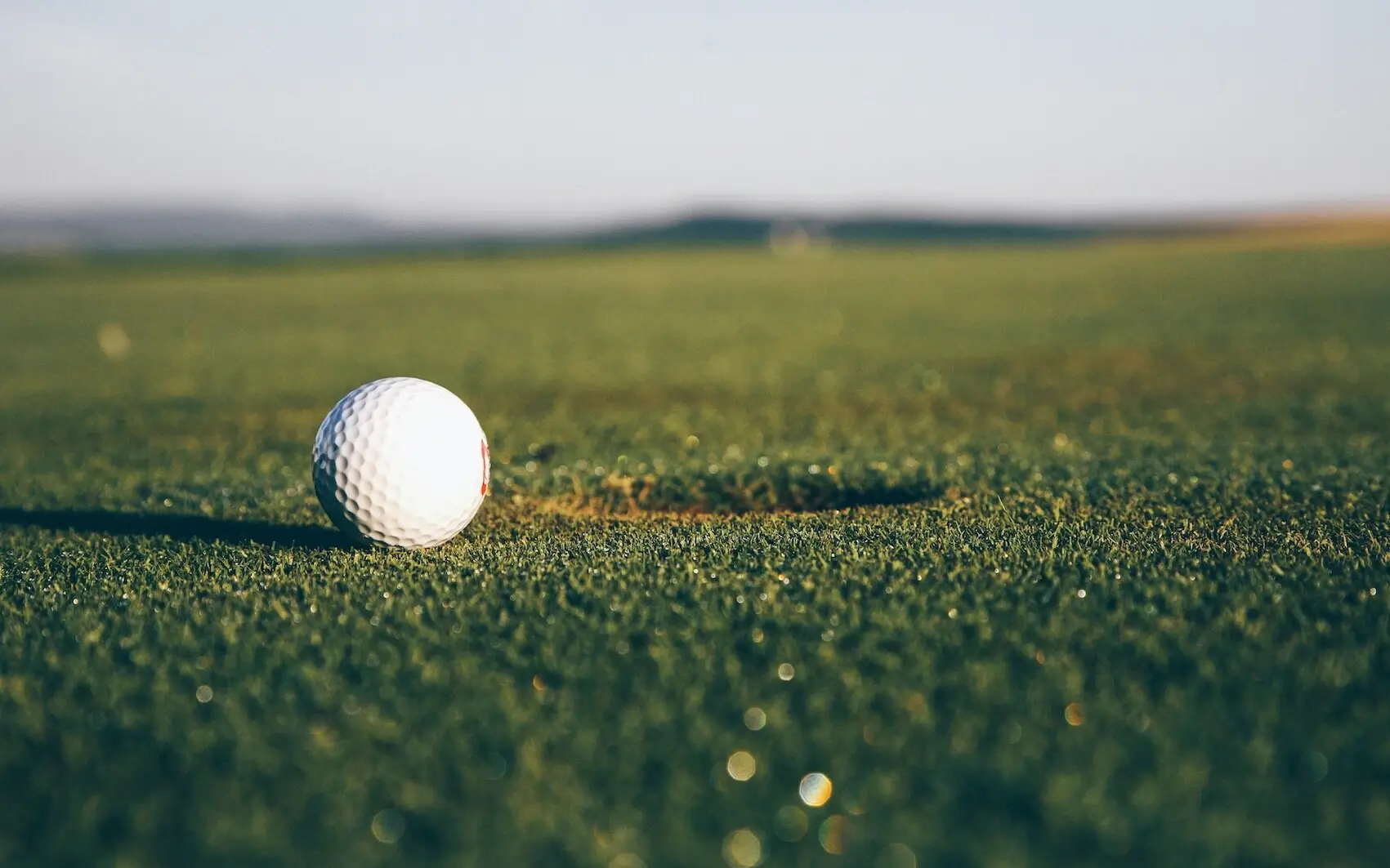 A golf ball lies on the grass in front of a hole.