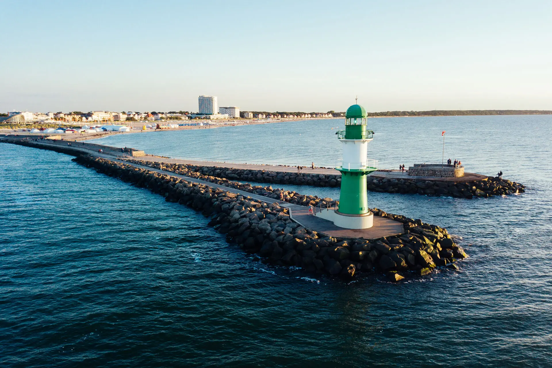 Grüner und weißer Leuchtturm auf Felsen im Wasser.