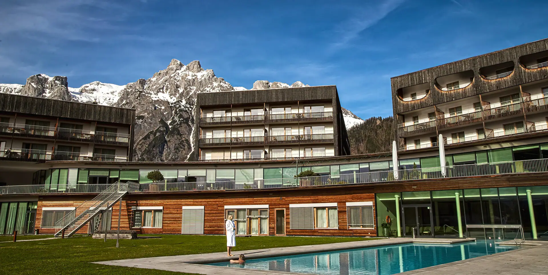 Eine Person steht vor einem Schwimmbecken und dem Hotel im Freien.