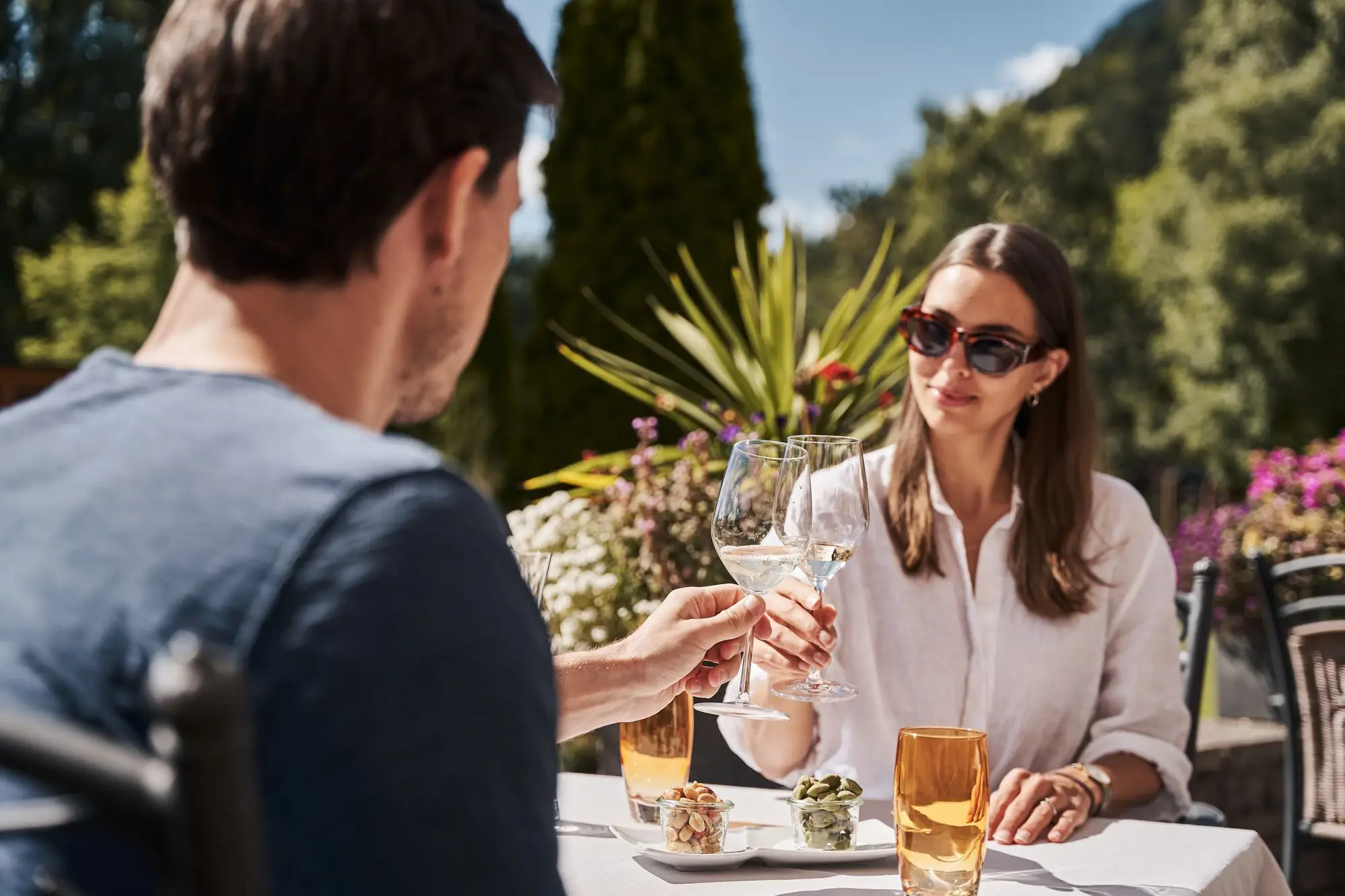 Ein Mann und eine Frau stoßen mit Weingläsern an einem Tisch im Freien an. 