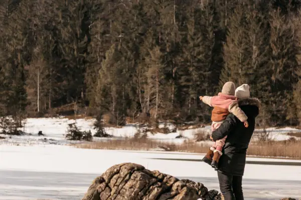 Ein Mann trägt ein Kind auf seinem Rücken im Schnee.
