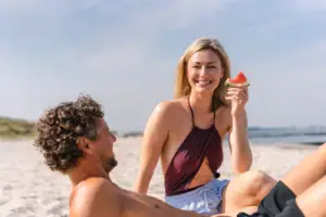 Eine Frau hält ein Stück Wassermelone, während sie am Strand sitzt.
