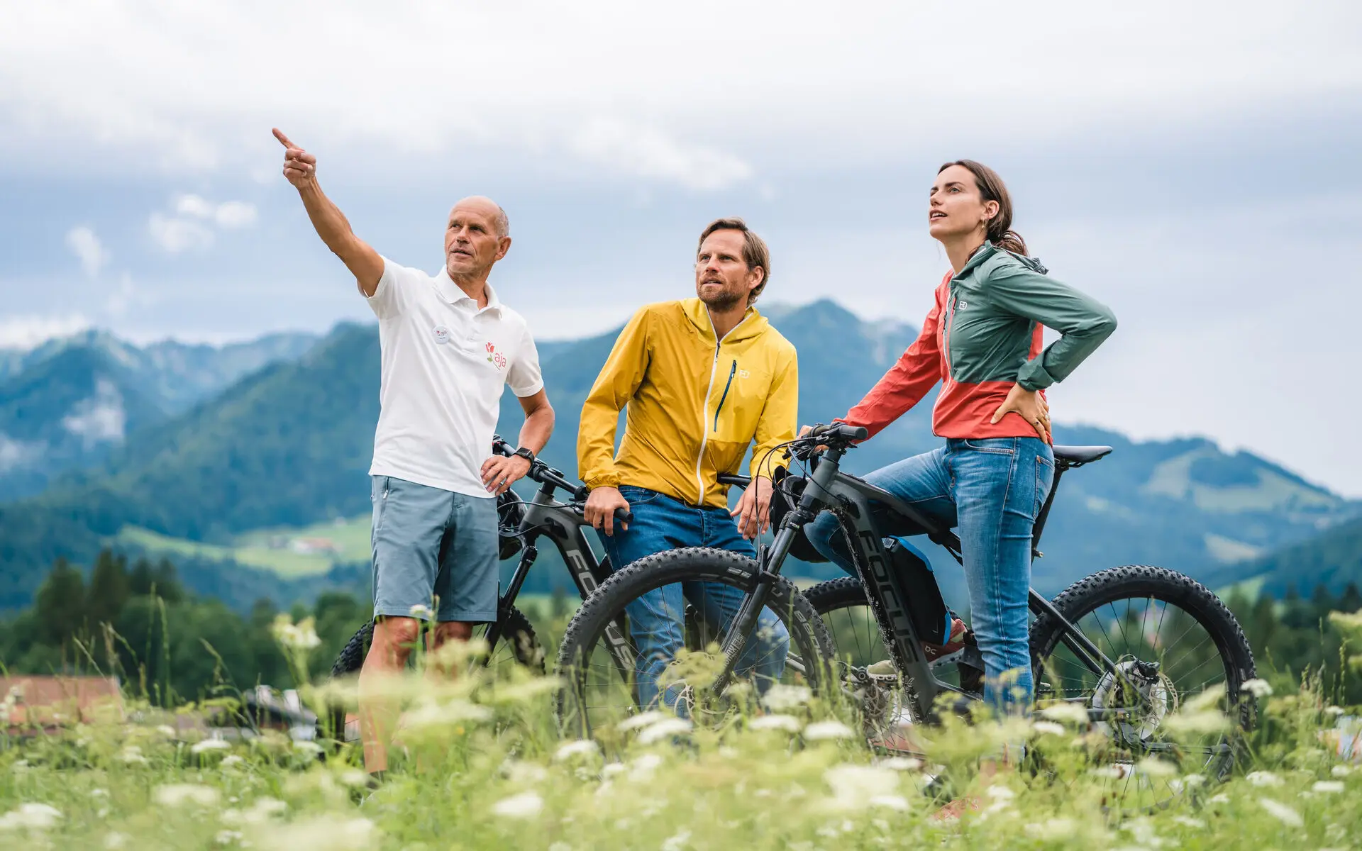 Drei Personen mit E-Bikes, im Hintergrund ist eine Berglandschaft