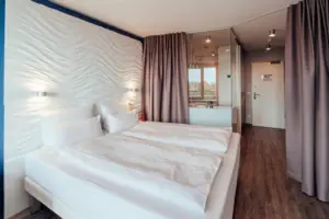 Bett mit weißen Laken und einem Vorhang im Hintergrund.