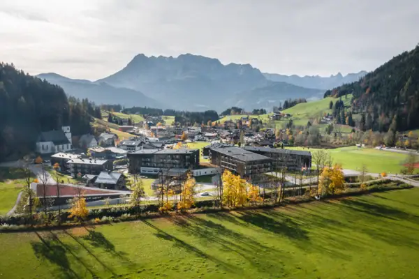 Stadt im Tal mit Bergen im Hintergrund, umgeben von Graslandschaft und Bäumen.