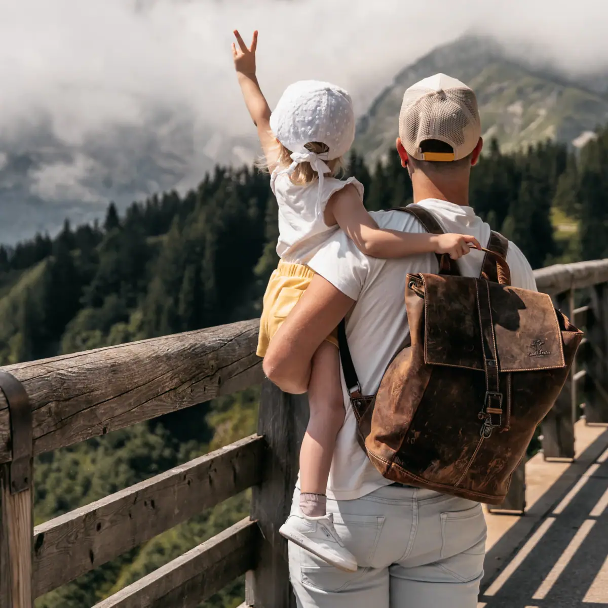 Ein Mann und ein Kind stehen auf einem Holzgeländer und blicken auf Berge.