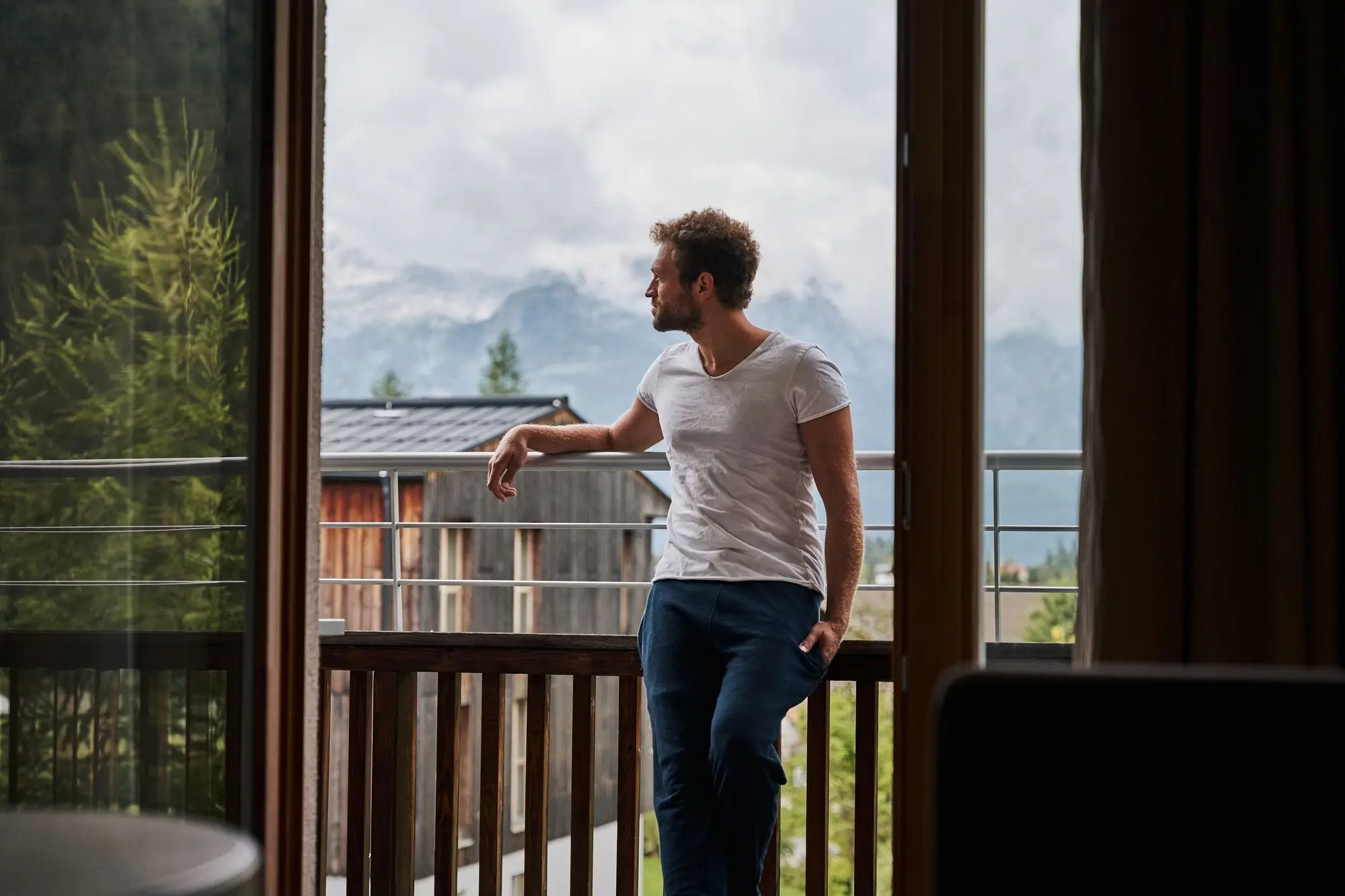 Mann lehnt an einem Geländer und blickt von einem Balkon auf eine Bergkette.