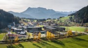 Blick auf eine Stadt im Tal mit umliegenden Bergen und einer Bahnlinie im Vordergrund.