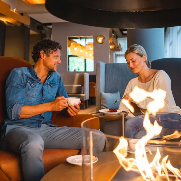 Restaurant und Bar im aja Warnemünde Ein Mann und eine Frau sitzen auf einem Stuhl und essen an einem Kamin.