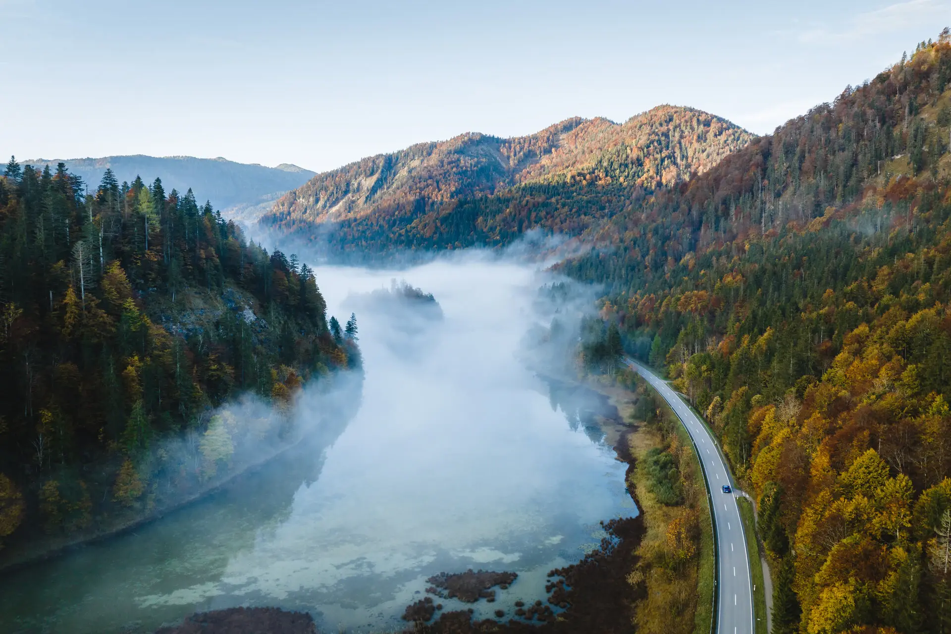 Straße und Fluss umgeben von Nebel in einer herbstlichen Landschaft.