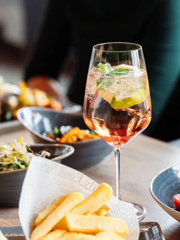 Ein Glas Getränk mit Limette und Minzblatt vor einer Schüssel Essen.