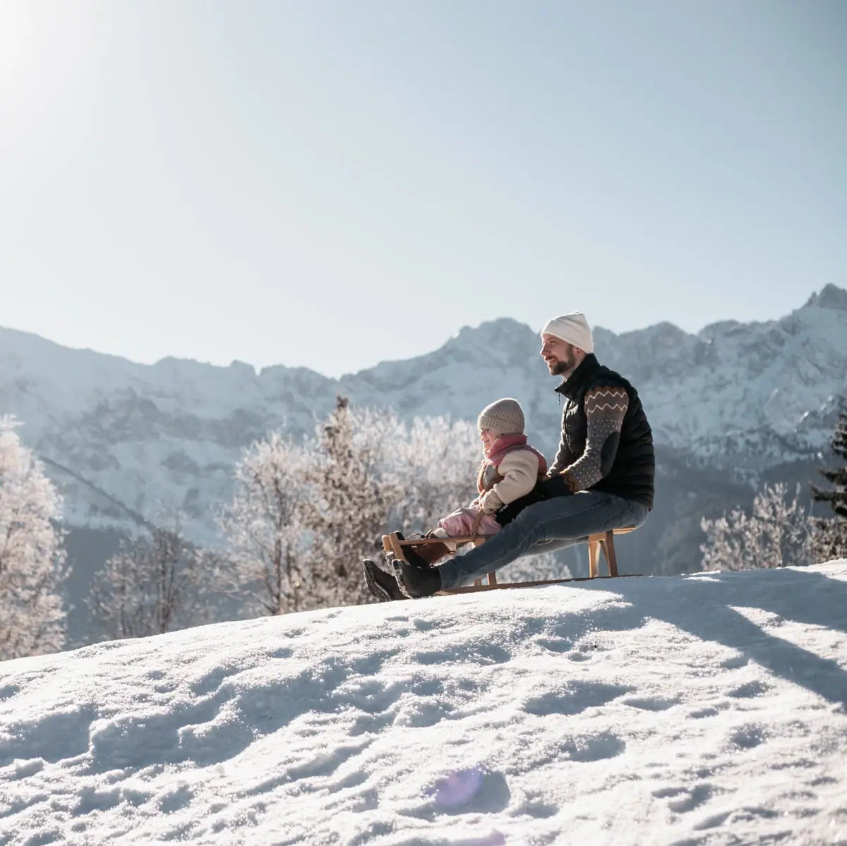 Ein Mann und ein Kind sitzen auf einer Bank im Schnee.