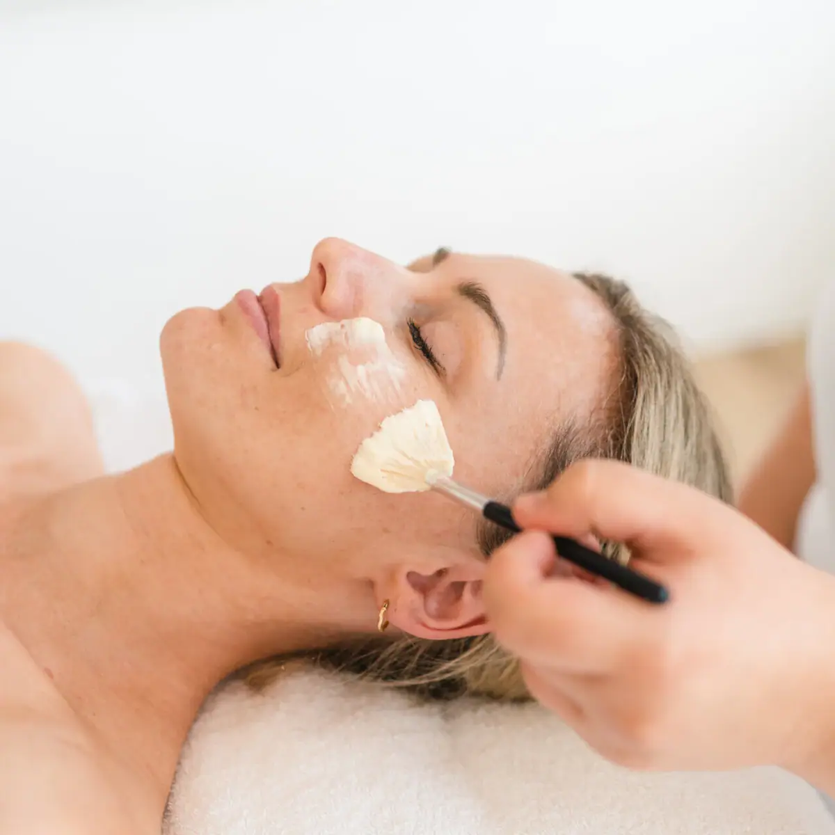 Gesichtsanwendung Eine Frau liegt entspannt, während ein Pinsel über ihr Gesicht geführt wird.