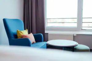 Blaues Sofa mit Kissen und rundem Tisch vor einem Fenster.