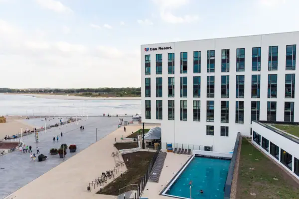 aja Hotel Travemünde Ein Gebäude mit einem Pool und Menschen, die herumlaufen.