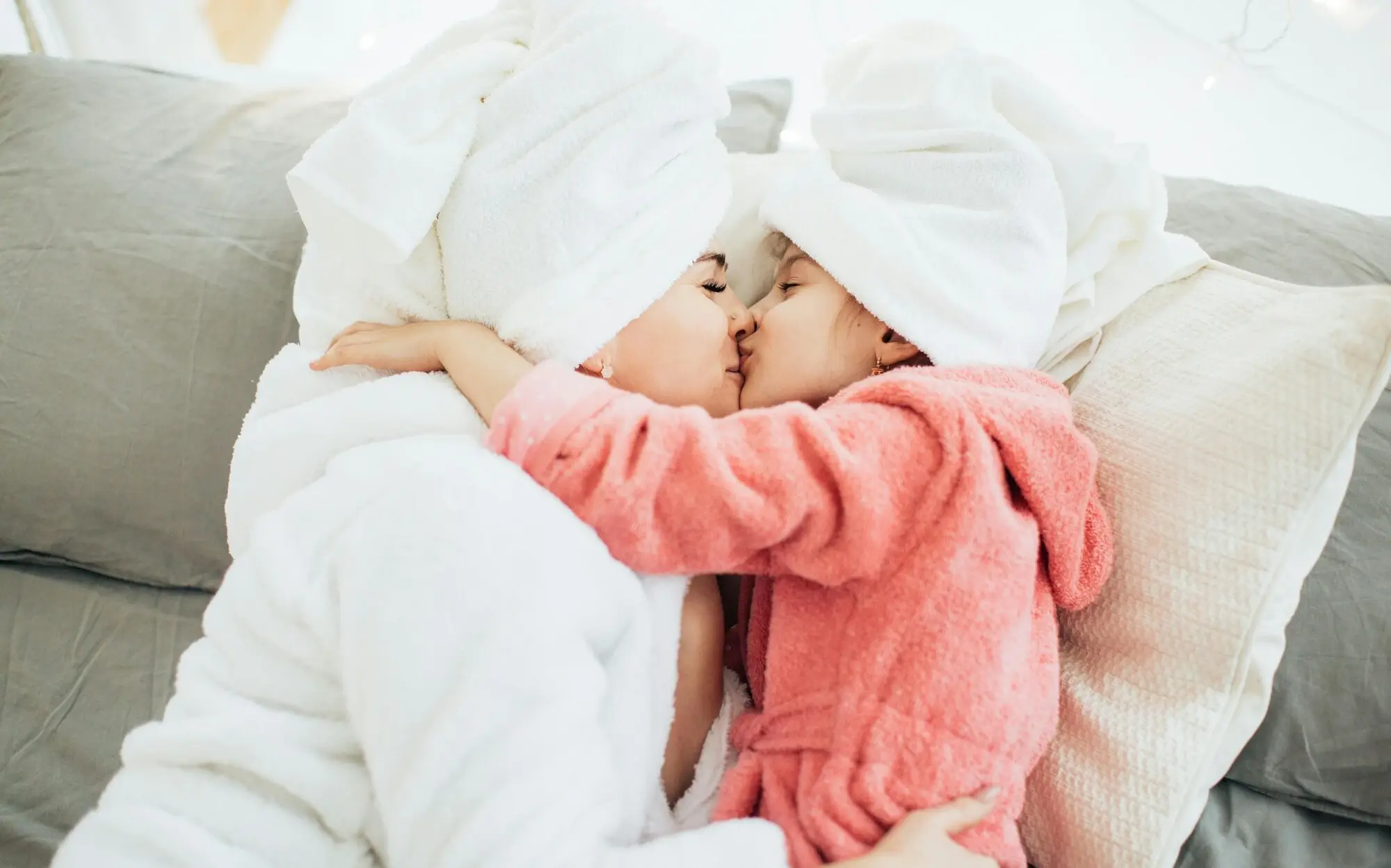 A mother kisses her daughter on the nose while they are both in their bathrobes.