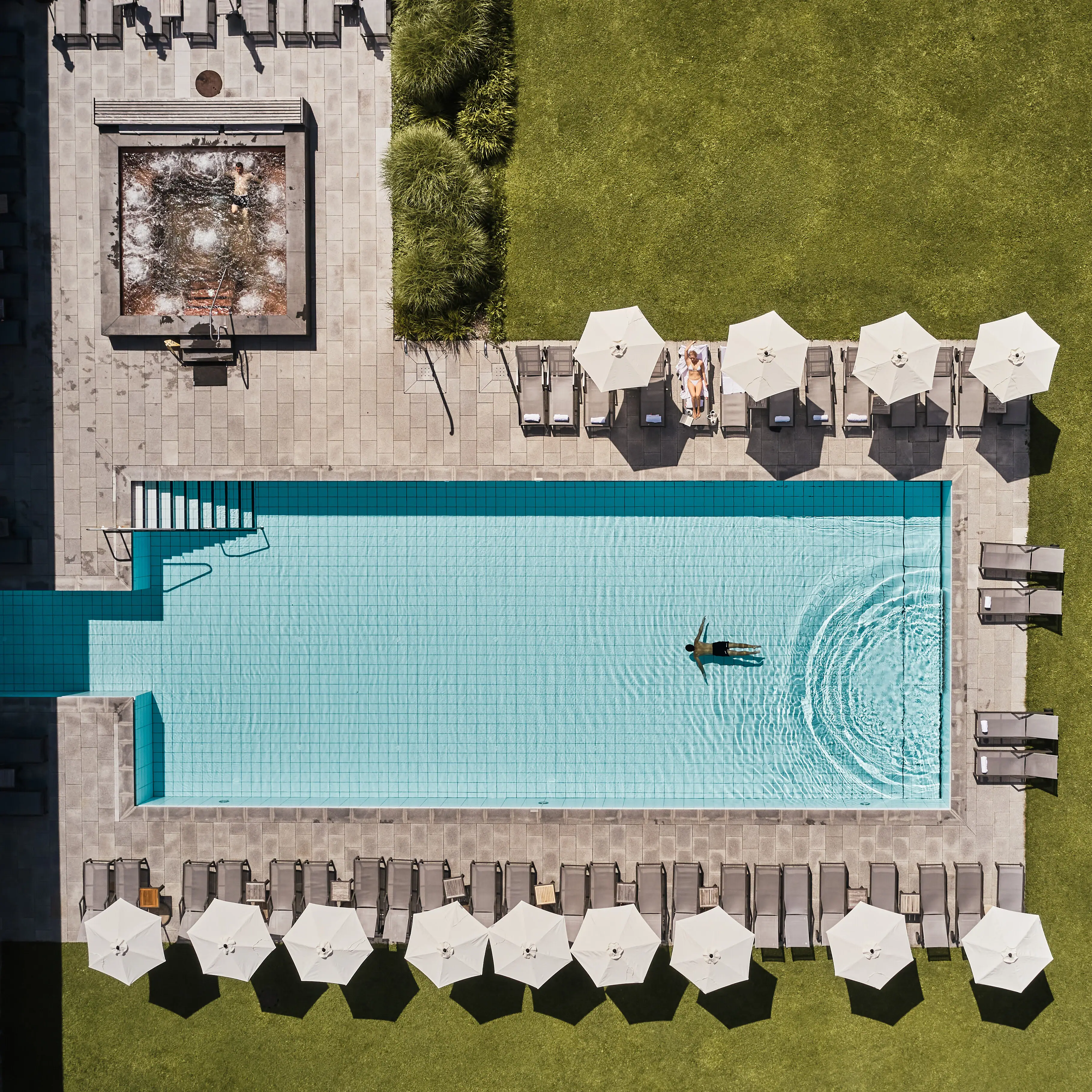 Außenpool Werfenweng Ein Schwimmbecken mit Sonnenschirmen und Gras.