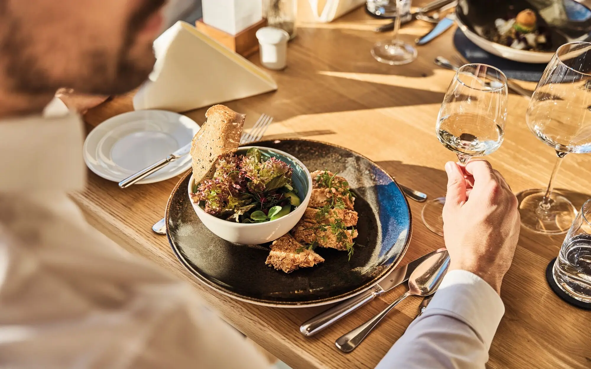 Mann isst Salat und trinkt ein Glas Wein am Tisch.