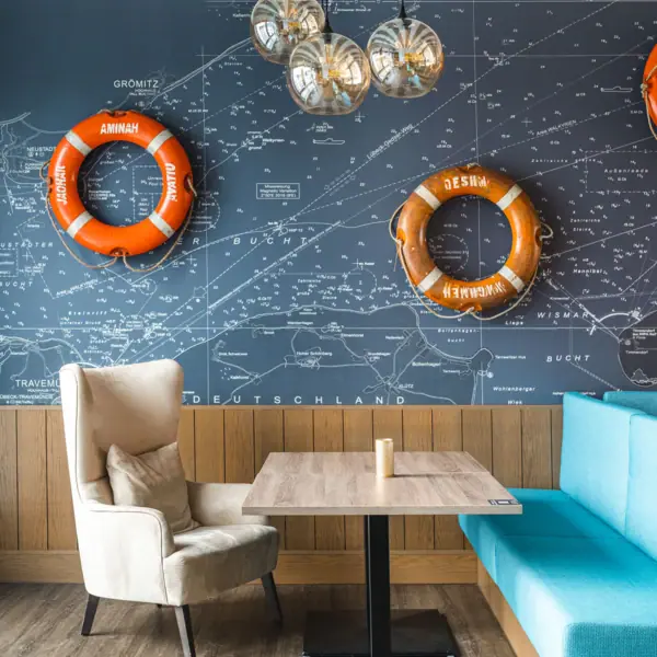 JEDERMANNS Restaurant Grömitz Ein Tisch und Stühle mit einem blauen Sofa und orangefarbenen Rettungsringen an der Wand.