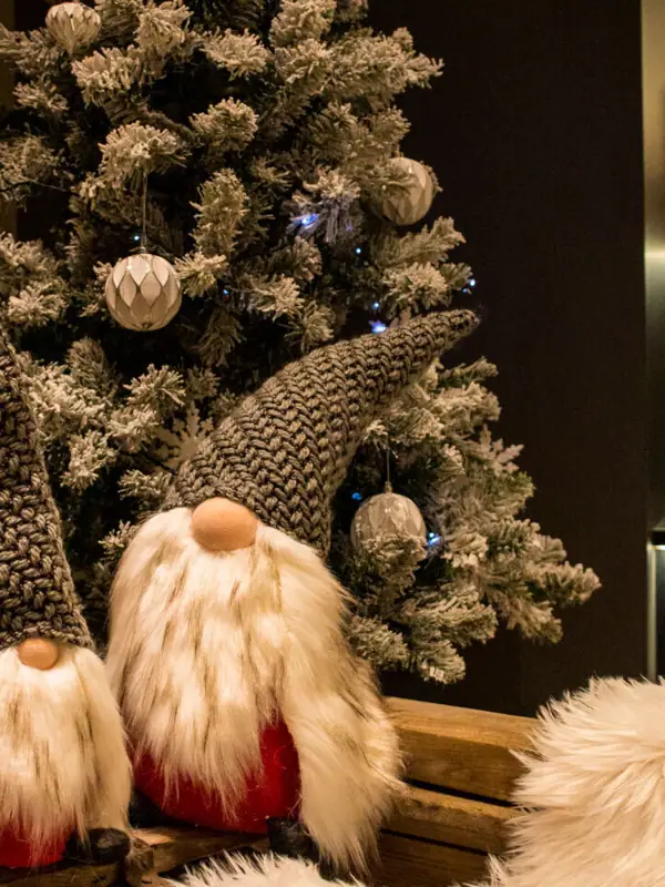 Zwei Wichtel sitzen auf einer Bank neben einem Weihnachtsbaum.