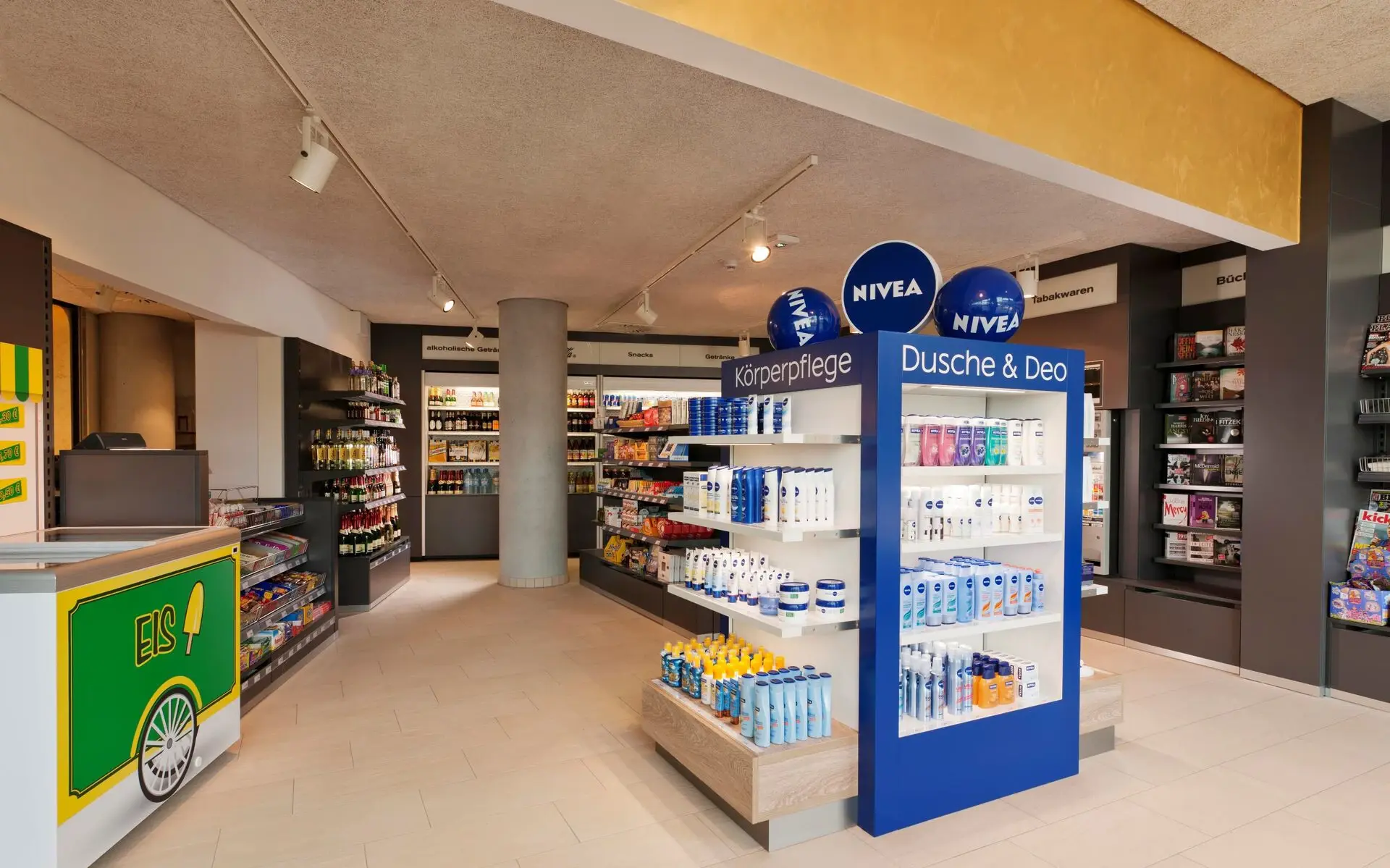 In einem Verkaufsraum mit hellem Holzboden und weißen Wänden sind diverse NIVEA Produkte in den Regalen zu erkennen. An der Decke im Hintergrund hängen blaue und weiße Luftballons mit dem NIVEA Logo bedruckt und links im Vordergrund ist ein weißer Verkaufstresen zu sehen.