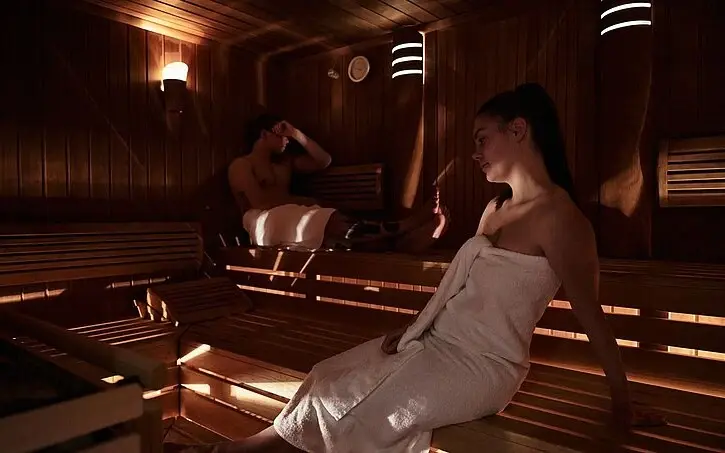 A woman and man sitting in a sauna with white towels..